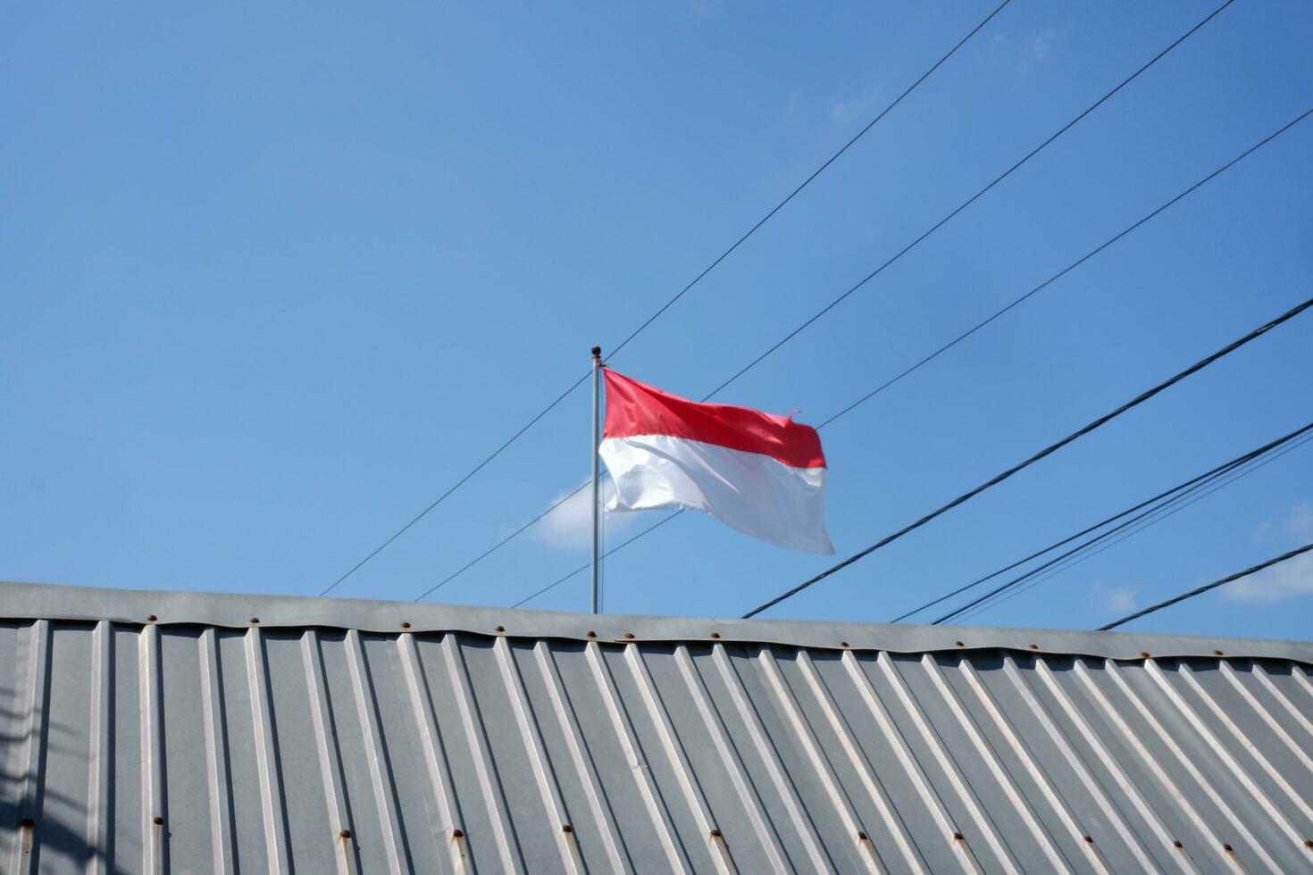 The red and white Indonesian flag is flying against a background of blue sky and cables photo