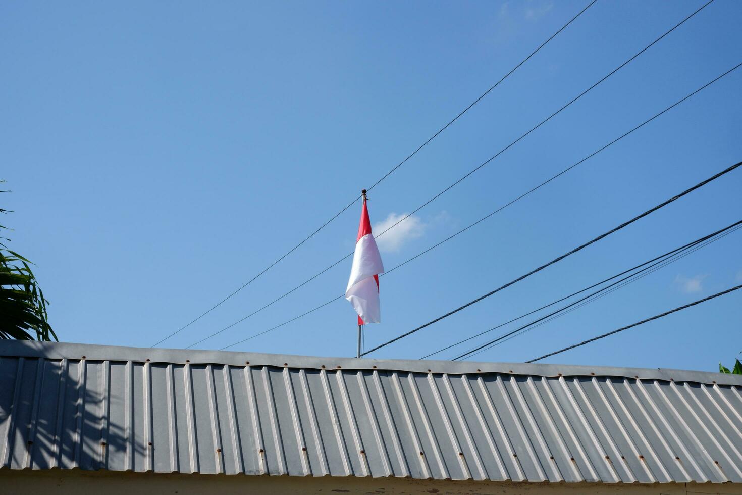 The red and white Indonesian flag is flying against a background of blue sky and cables photo