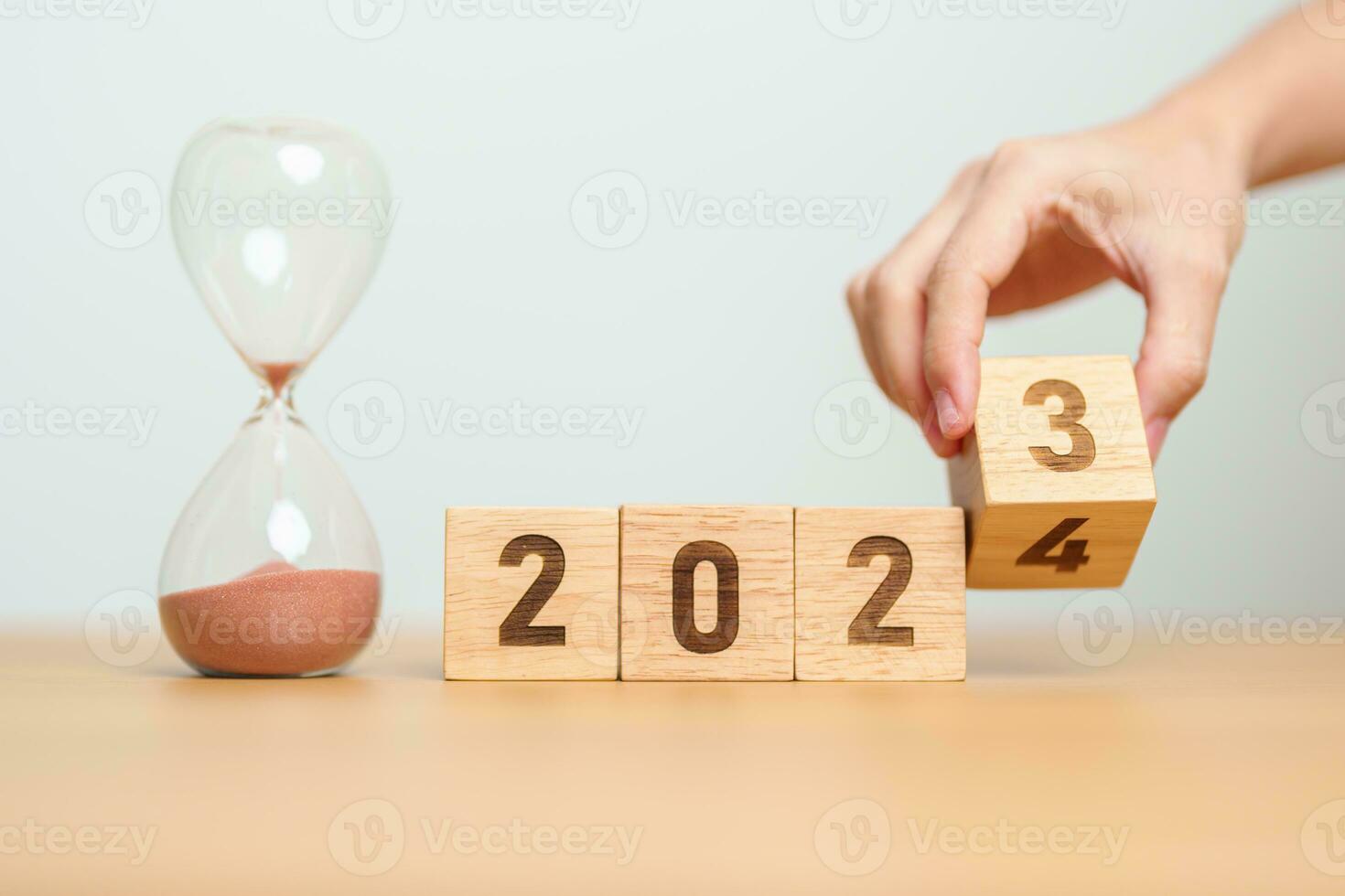 hand flipping block 2023 to 2024 text with hourglass on table. Resolution, time, plan, goal, motivation, reboot, countdown  and New Year holiday concepts photo