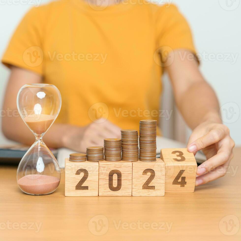 Happy New Year with sandglass and flipping 2023 change to 2024 block. Resolution, Goals, Plan, Action, Money Saving, Retirement fund, Pension, Investment and Financial concept photo