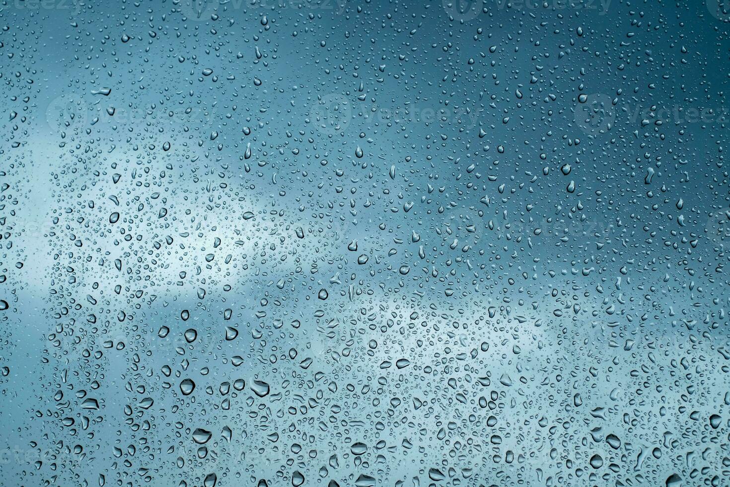 Rain drops on window glasses surface with blurred blue sky background. Natural backdrop of raindrops. Abstract overlay for design. The concept of bad rainy weather.rainy season photo