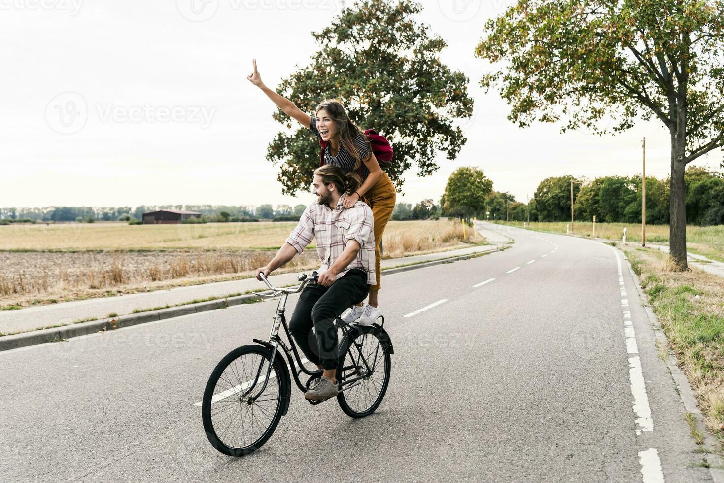 Happy young couple riding together on one bicycle on country road photo