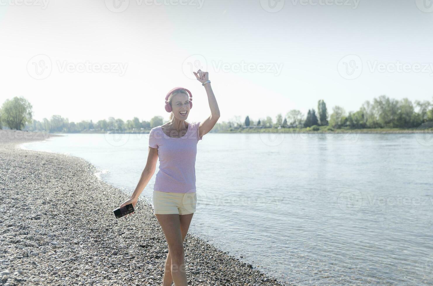 Happy mature woman listening to music with headphones at the riverside photo