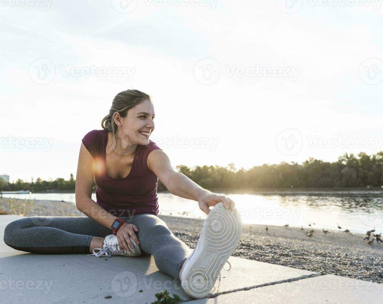 Young woman sitting on ground at the river, warming up for training photo