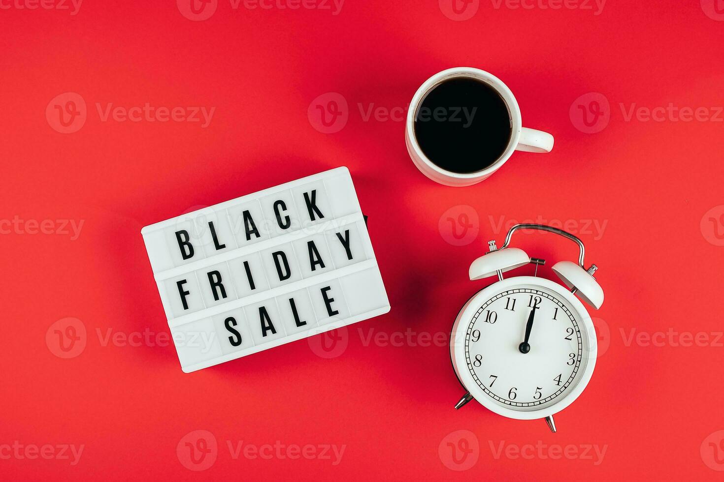 Black friday sale word on lightbox, cup of coffee, alarm on red background table. Flat lay photo