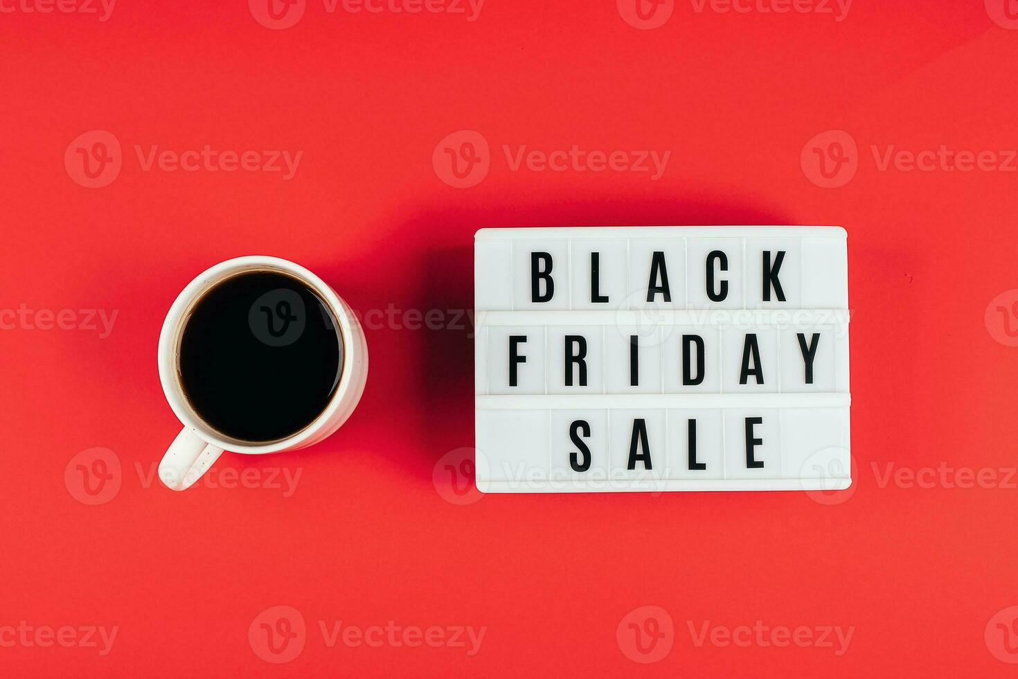 Black friday sale word on lightbox and cup of coffee on red background table. Flat lay, top view photo