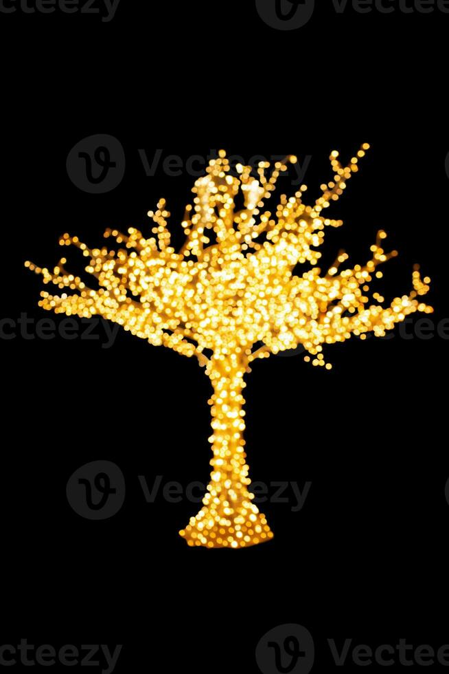 Blurred lights of yellow garland on defocused tree on black isolated background. Concept of Merry Christmas and Happy New Year, city decoration on another holidays. Copy space photo