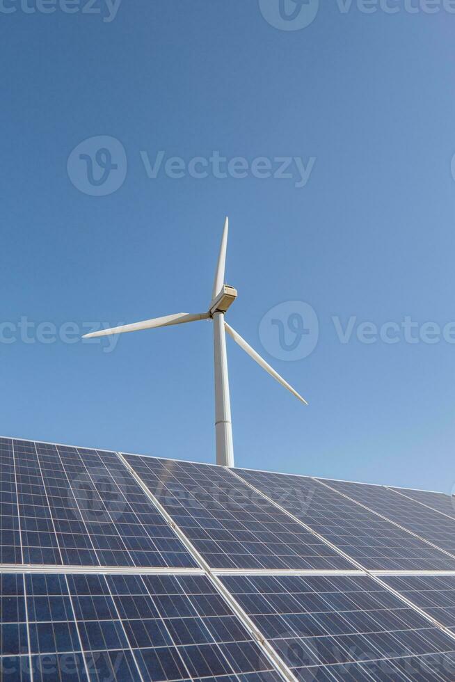 Solar panels and wind turbine against blue sky photo