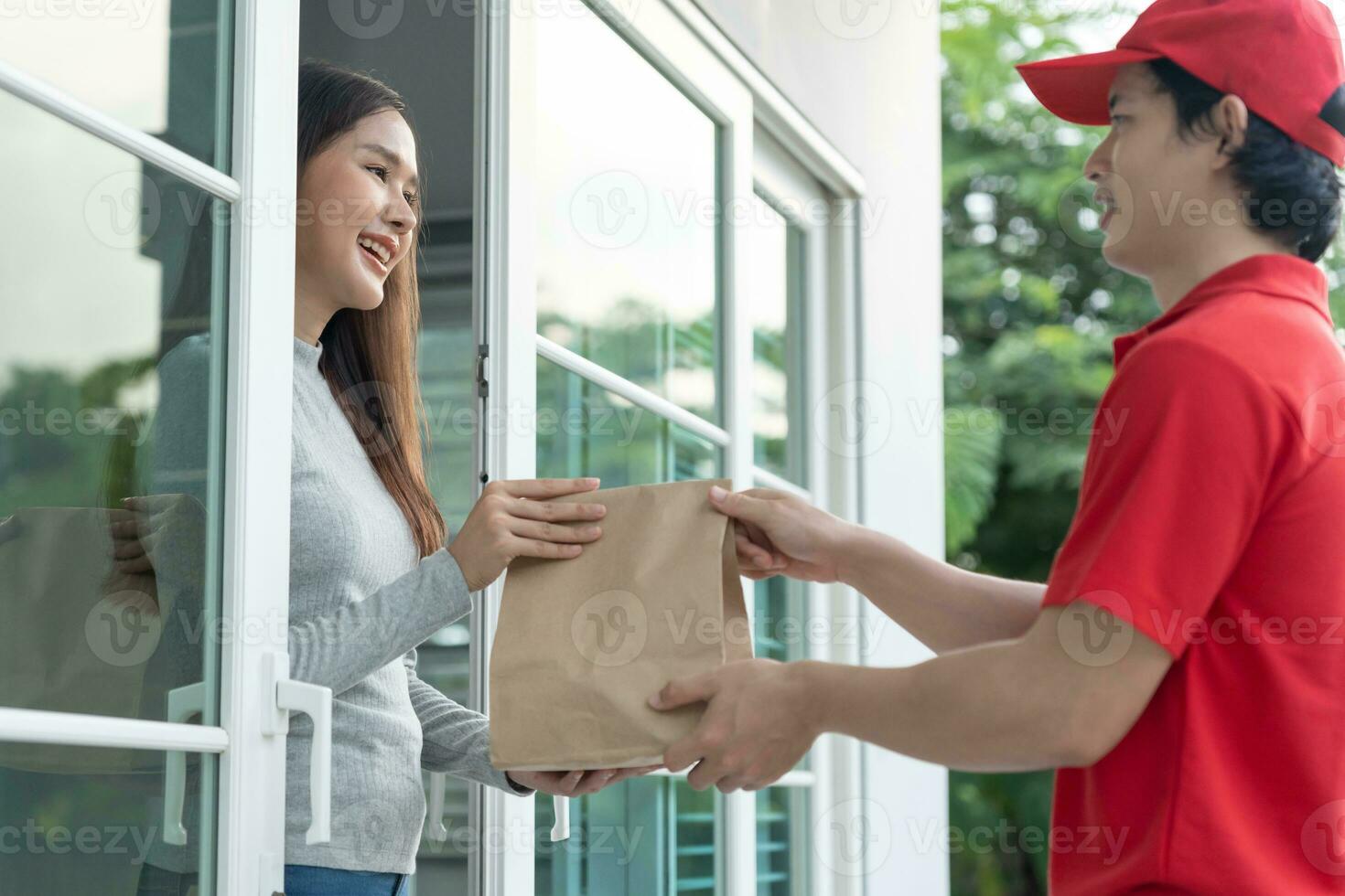 Happy smiling Asian woman receives paper bag parcel of food from courier front house. Delivery man send deliver express. online shopping, paper container, takeaway, postman, delivery service, packages photo