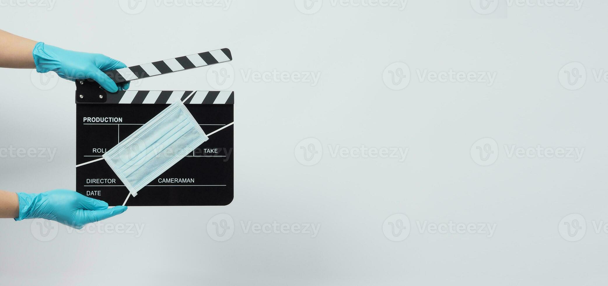 Hand is wear blue gloves and hold black Clapper board or movie slate with face mask. it use in video production and cinema industry on white background. photo