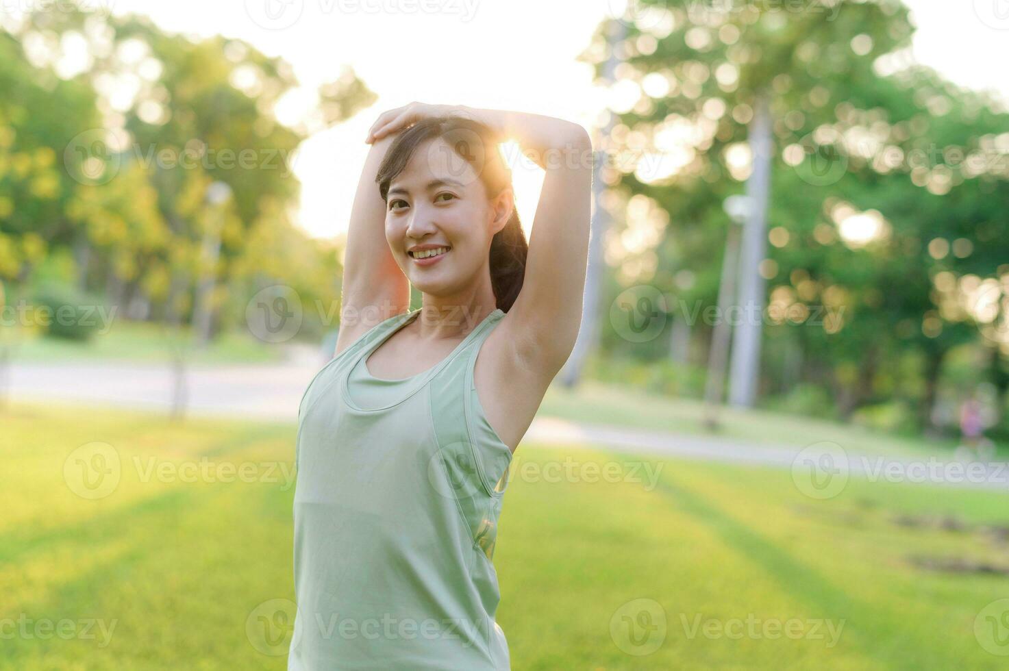 hembra persona que practica jogging. ajuste joven asiático mujer con verde ropa de deporte extensión músculo en parque antes de corriendo y disfrutando un sano exterior. aptitud corredor niña en público parque. bienestar siendo concepto foto