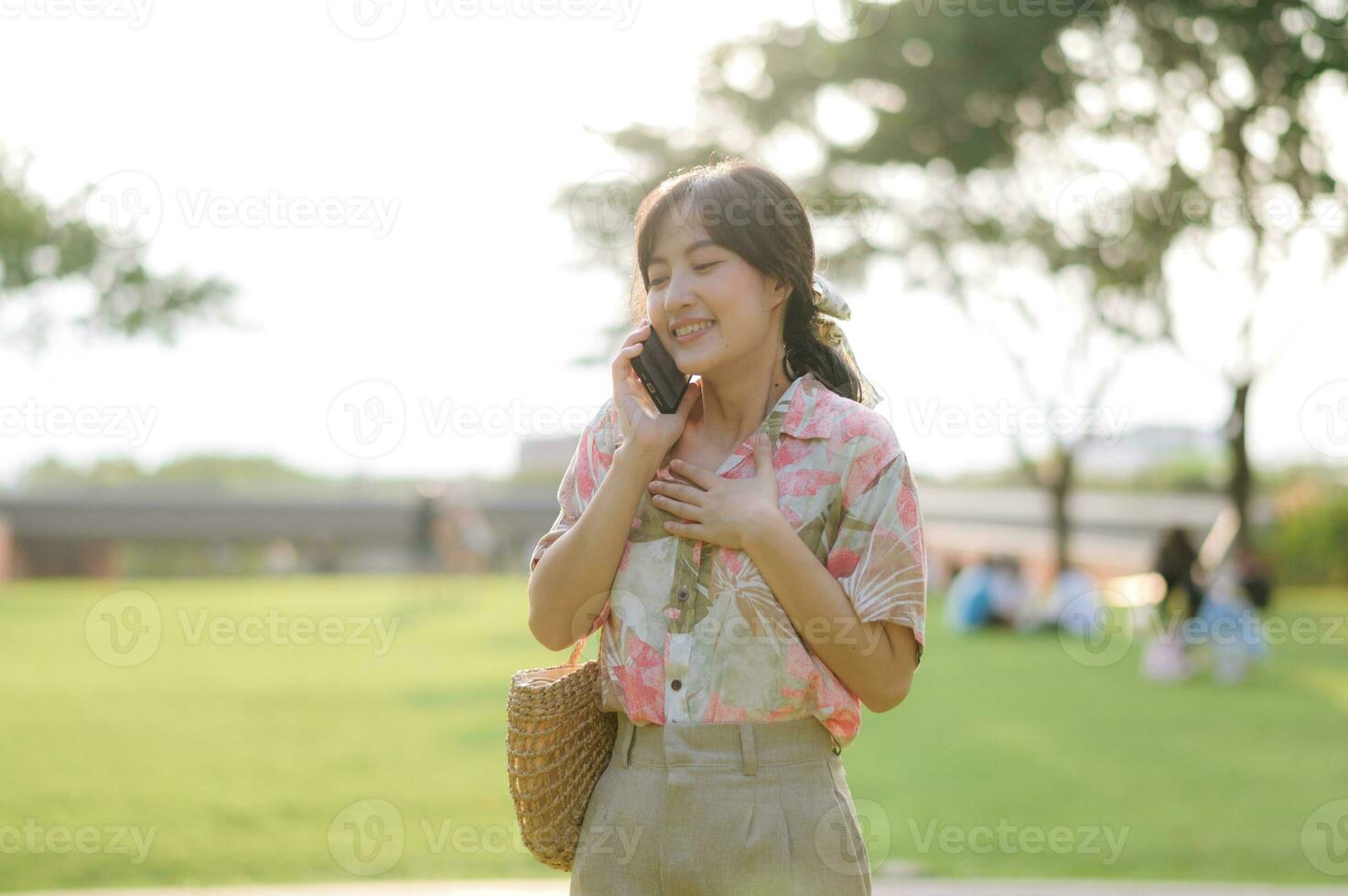 Portrait of asian young woman traveler with weaving basket, mobile phone on green public park background. Journey trip lifestyle, world travel explorer or Asia summer tourism concept. photo