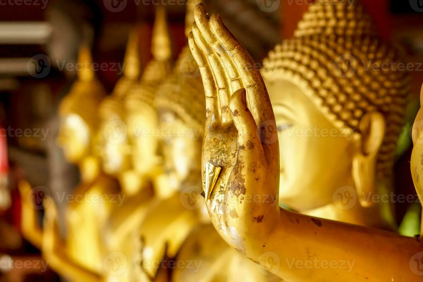 Closeup and crop hand of golden Buddha statue with a gold leaf on blurred golden Buddha statue stand strong line background photo