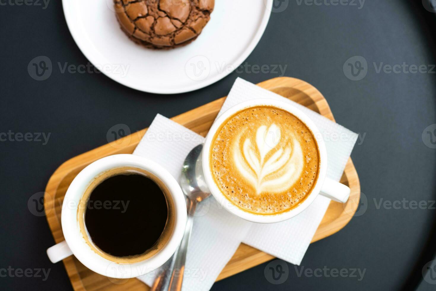 A cup of coffee and a cup of cappuccino with chocolate chip cookies on a black table. Top view. Coffee break. photo