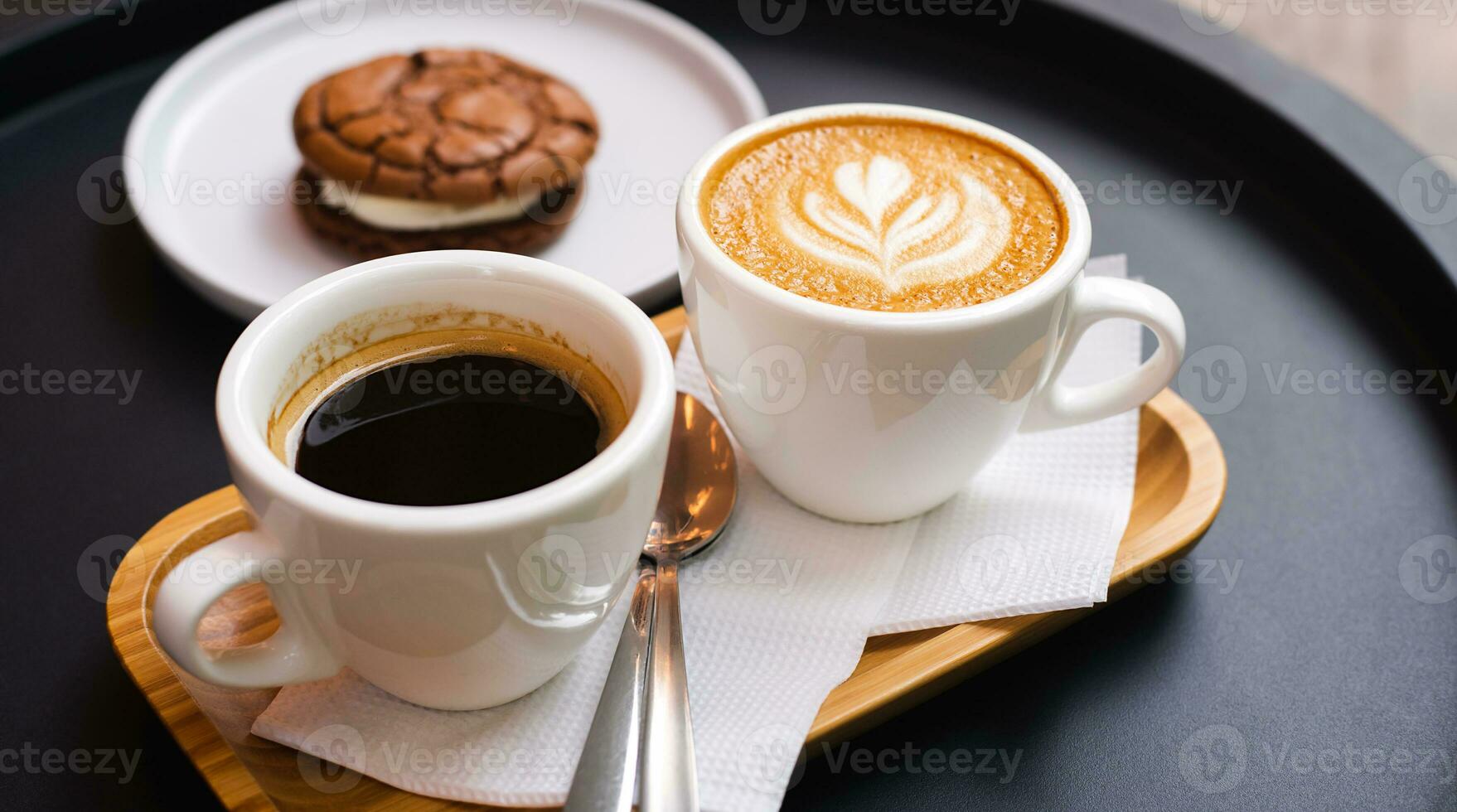A cup of cappuccino and cup of coffee with chocolate biscuit on the black table in cafe. Close-up. photo