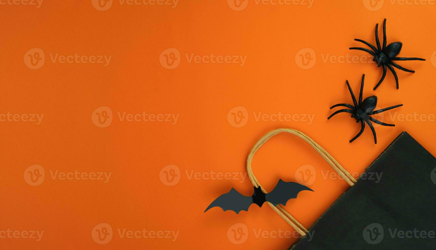 Paper black package, bat and spiders on orange background. Halloween shopping and sale concept. Flatlay composition. Banner. Place for text. photo