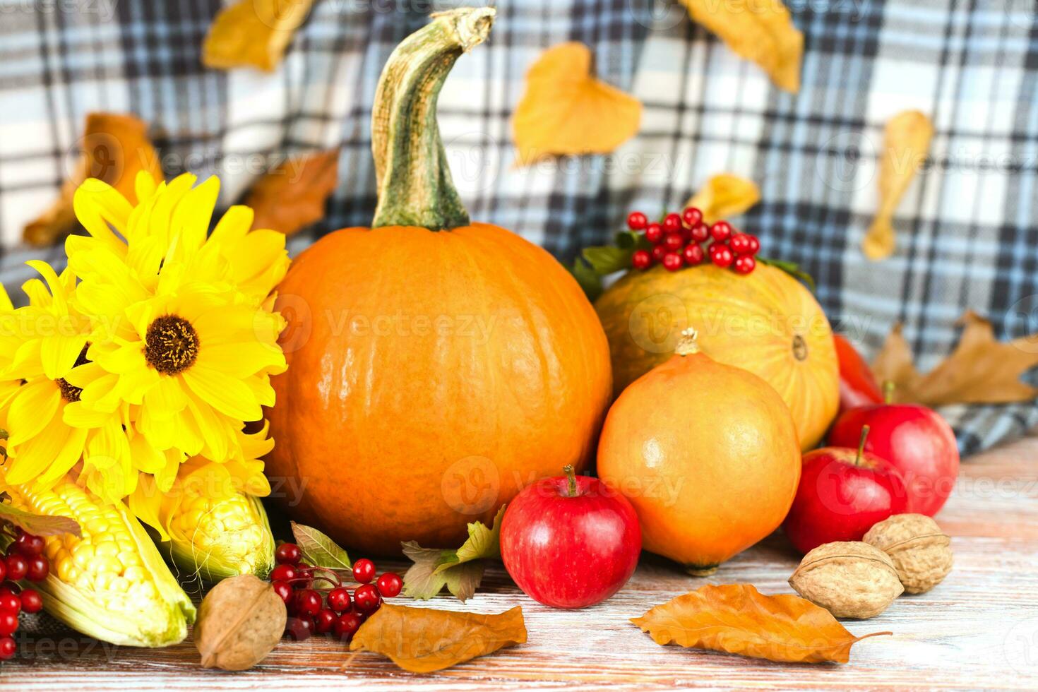 Happy Thanksgiving. Autumn composition with pumpkins, yellow flowers, various vegetables and autumn leaves on a wooden background. Festive autumn decor. Close-up. photo