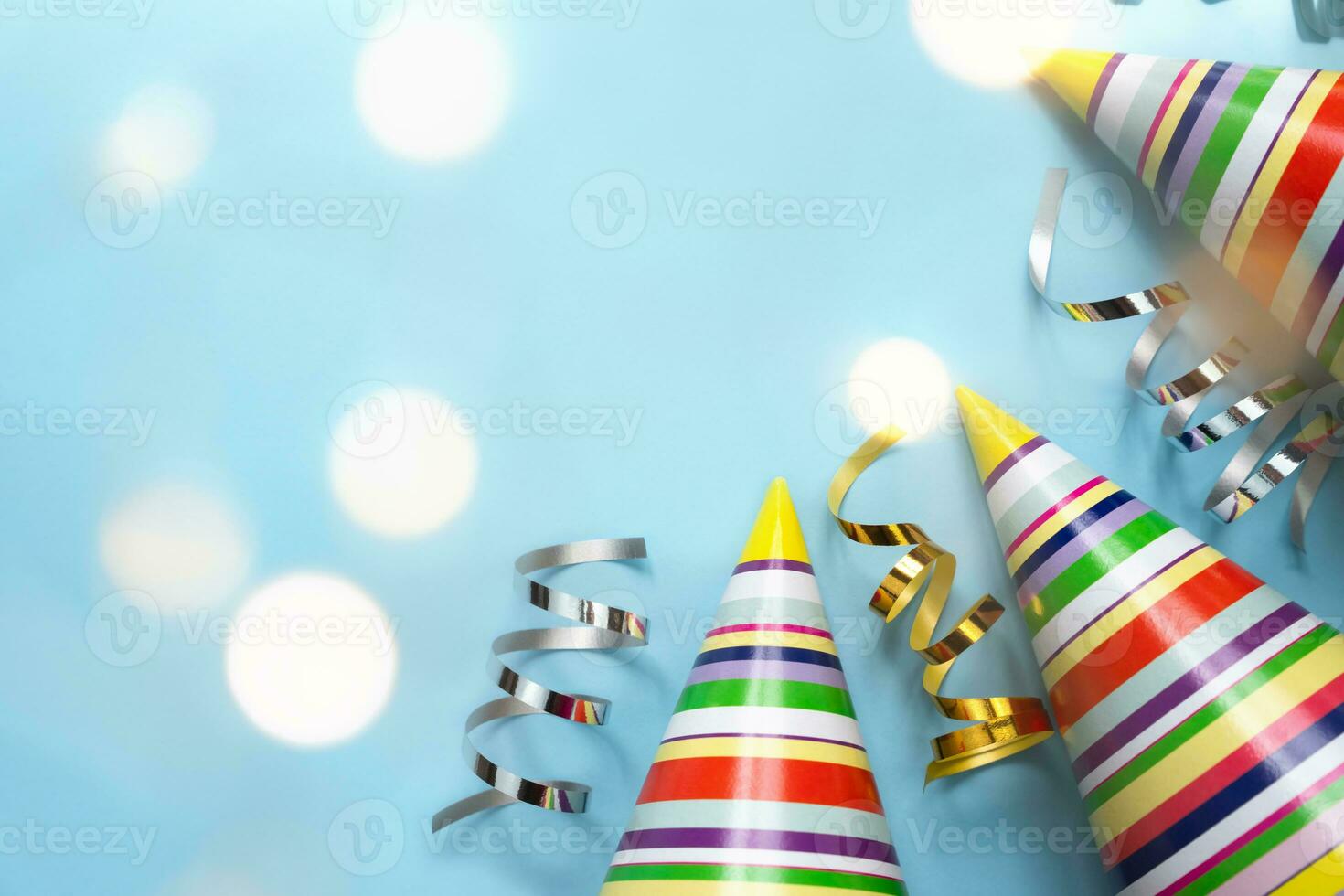Bright colored party hats and holiday decor with beautiful bokeh on a blue background. Holidays concept. Top view. Copy space. photo