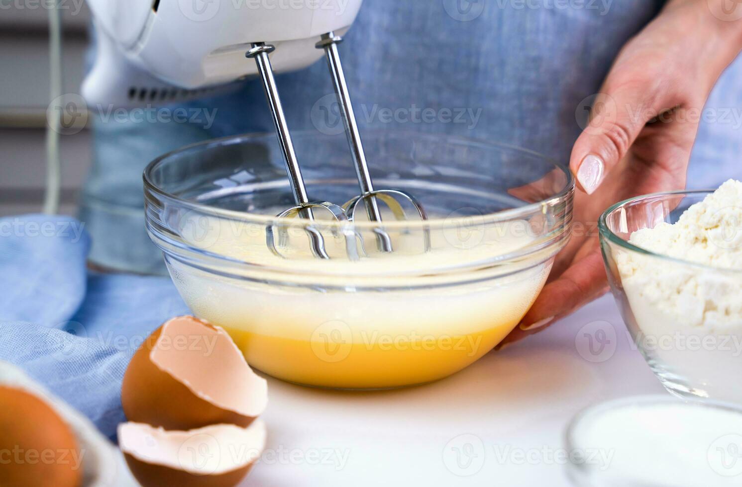 A young girl beats eggs with a mixer at the kitchen for making homemade cookies. Preparation process. Selective focus. photo