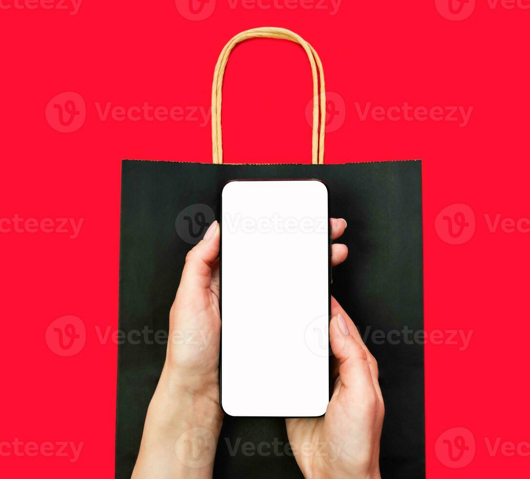 Woman's hands hold a smartphone with a blank screen on the background of a shopping bag. Mock up screen. Shopping and delivery with a mobile application. Top view. Flatlay. Copy space. photo