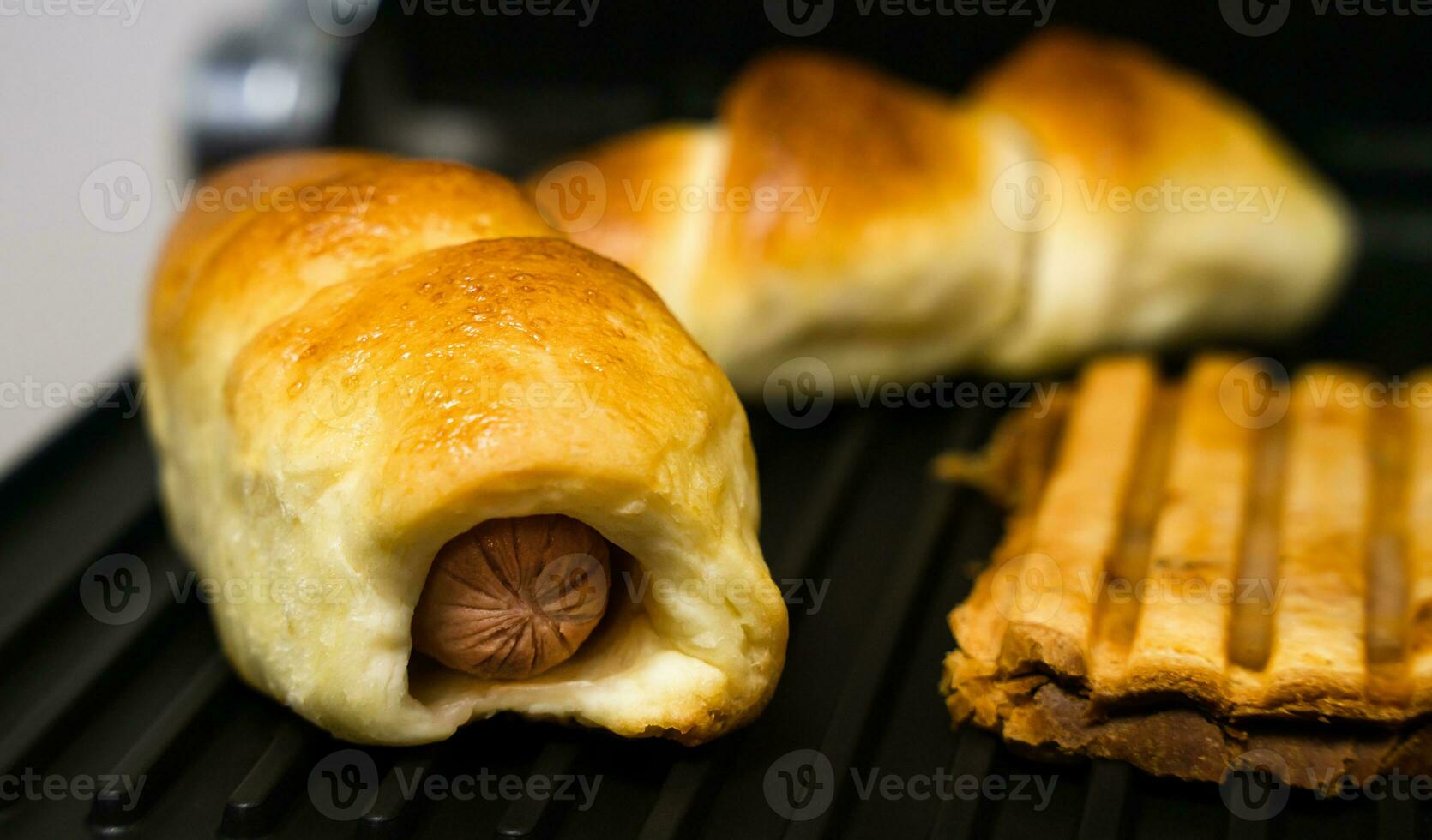 Sausages in dough and sandwiches are grilled for fast food breakfast or coffee break. Close-up. Selective focus. photo
