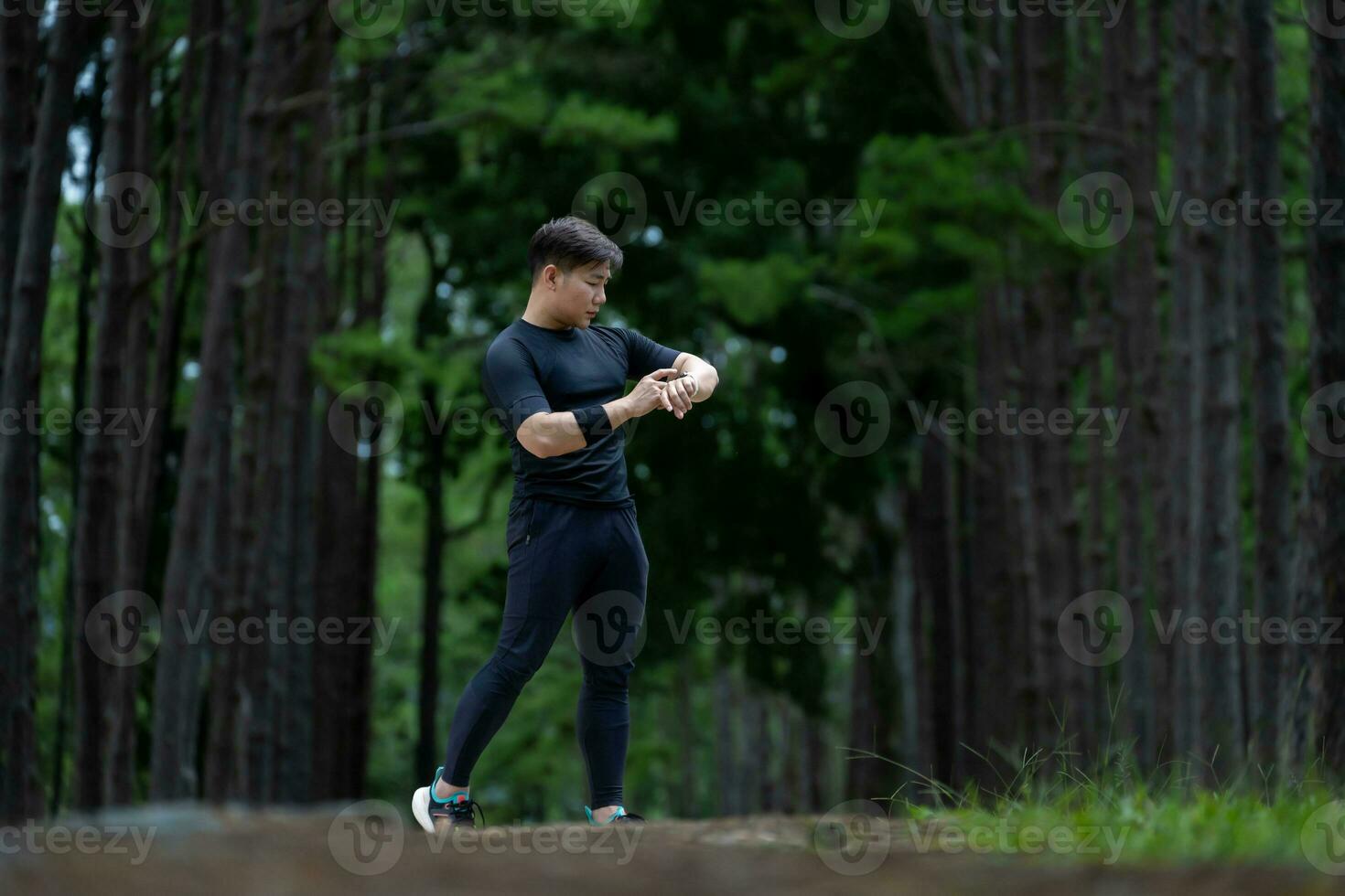 Asian trail runner is running outdoor in pine forest dirt road for exercise and workout activities training while checking smart watch on calories loss achieve healthy lifestyle and fitness photo