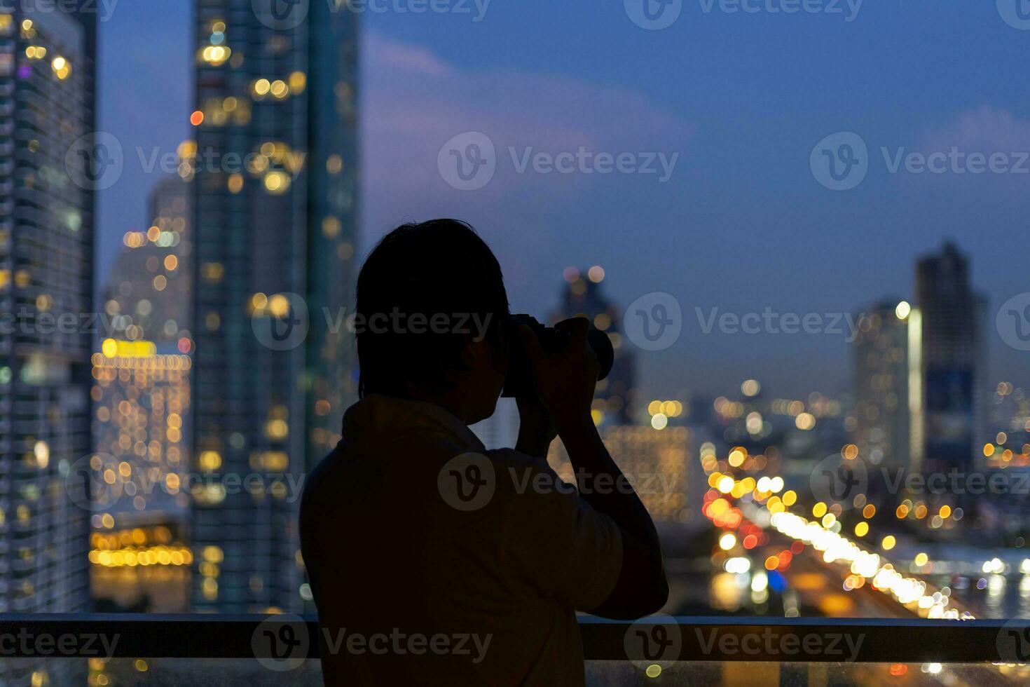 Photographer is taking cityscape photograph from the hotel balcony with evening street light at sunset scene for urban travel concept photo