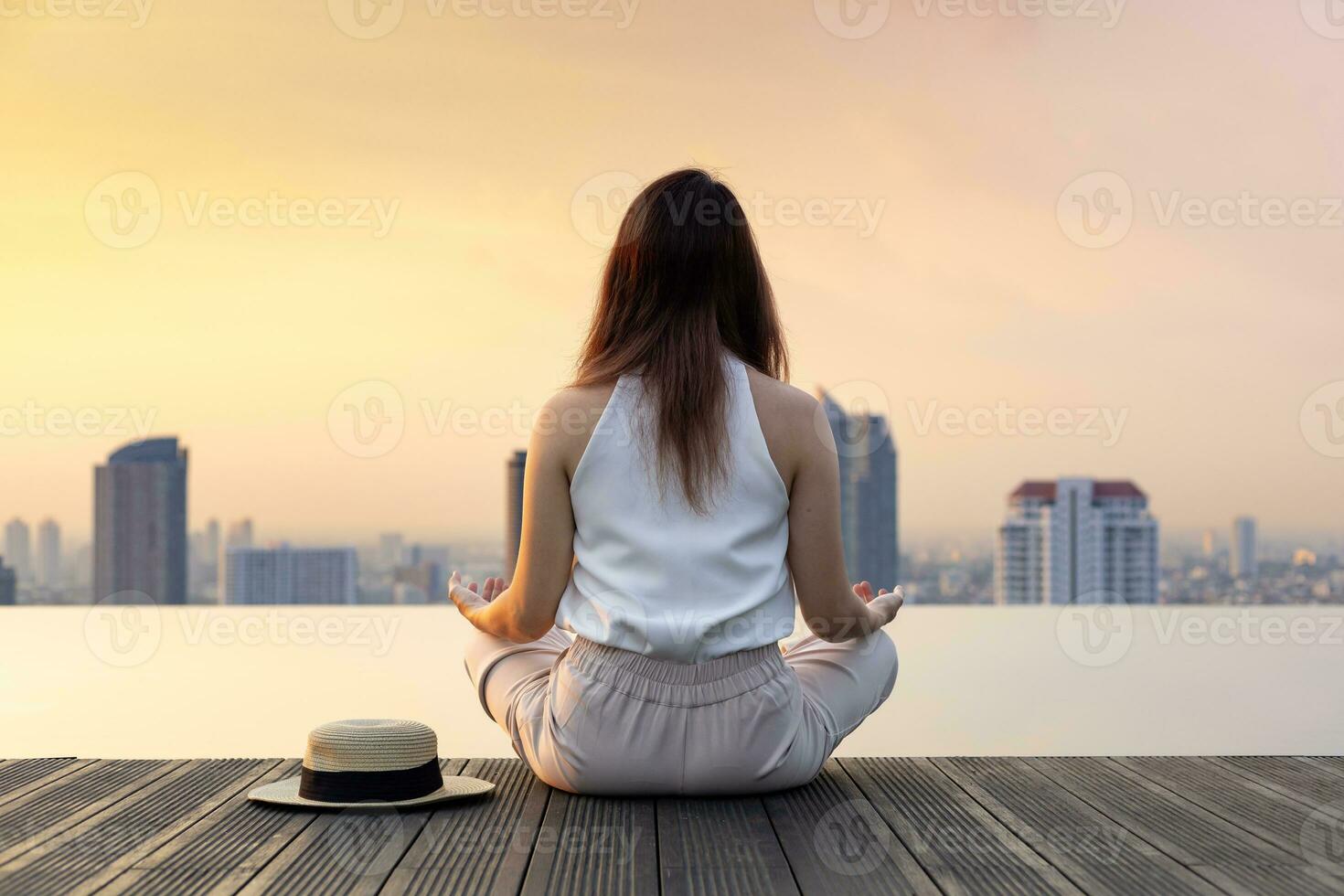 Back of woman relaxingly practicing meditation at the swimming pool rooftop with the view of urban skyline building to attain happiness from inner peace wisdom photo