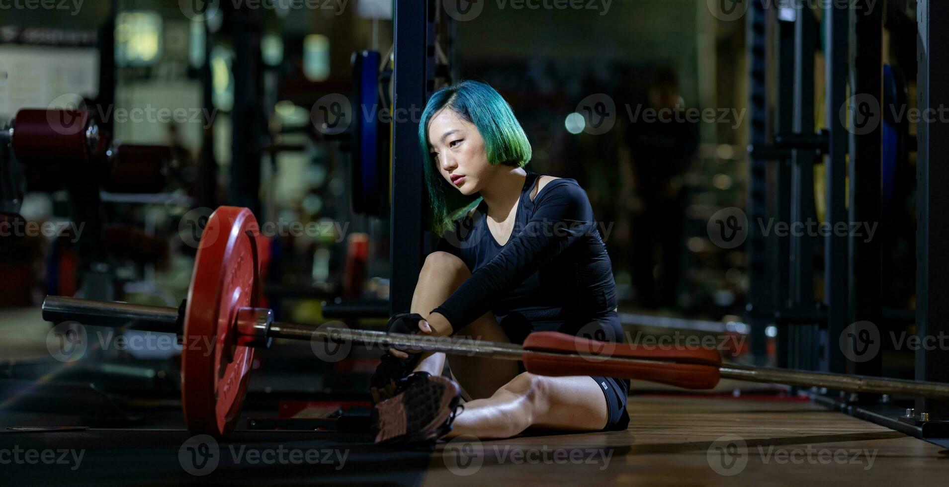 Asian woman is facing overtraining syndrome after weight training workout inside gym with dark background for exercising and fitness concept photo