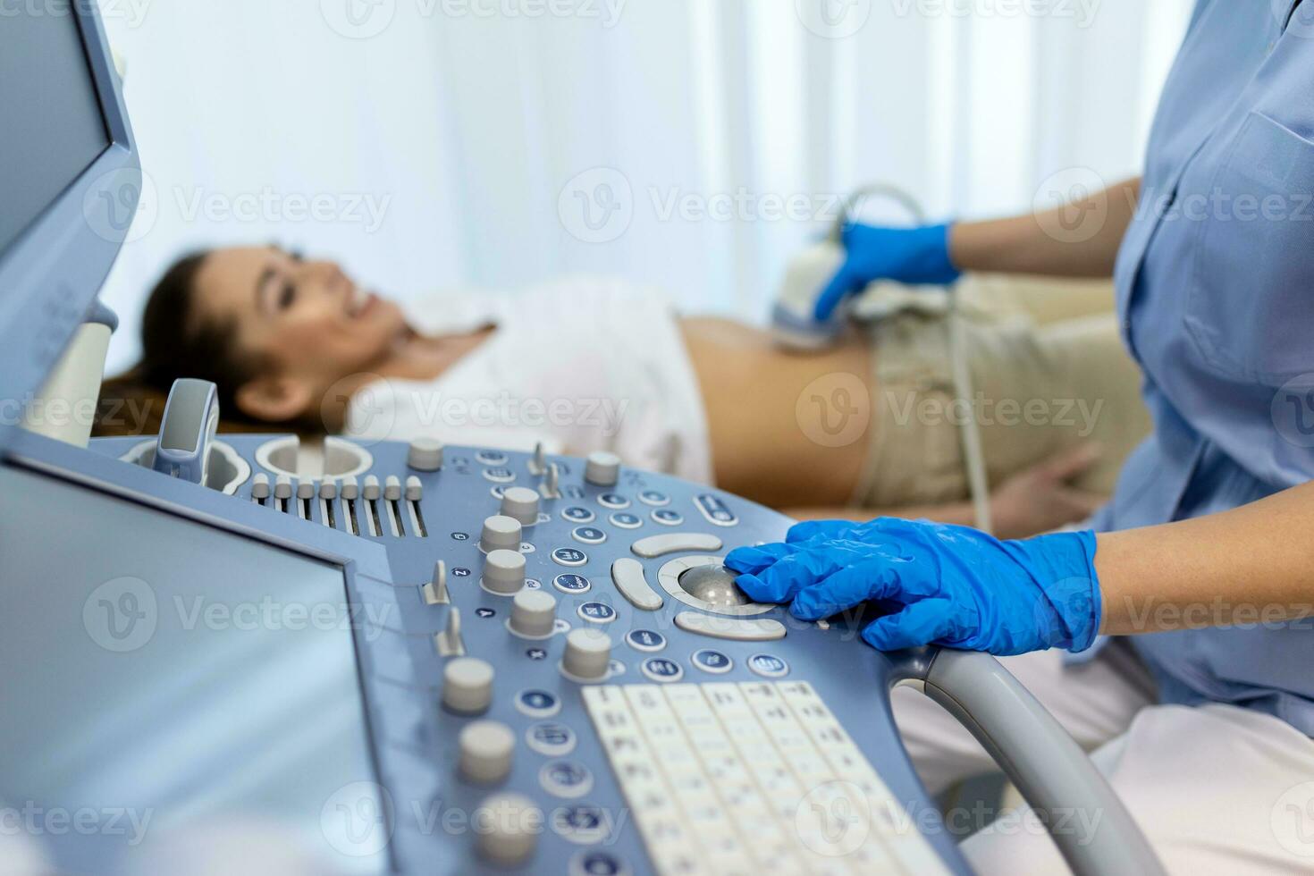 Side view portraits of gynecologist in white lab coat and sterile gloves using ultrasound scanner while examining female patient. woman lying on daybed on blurred background photo