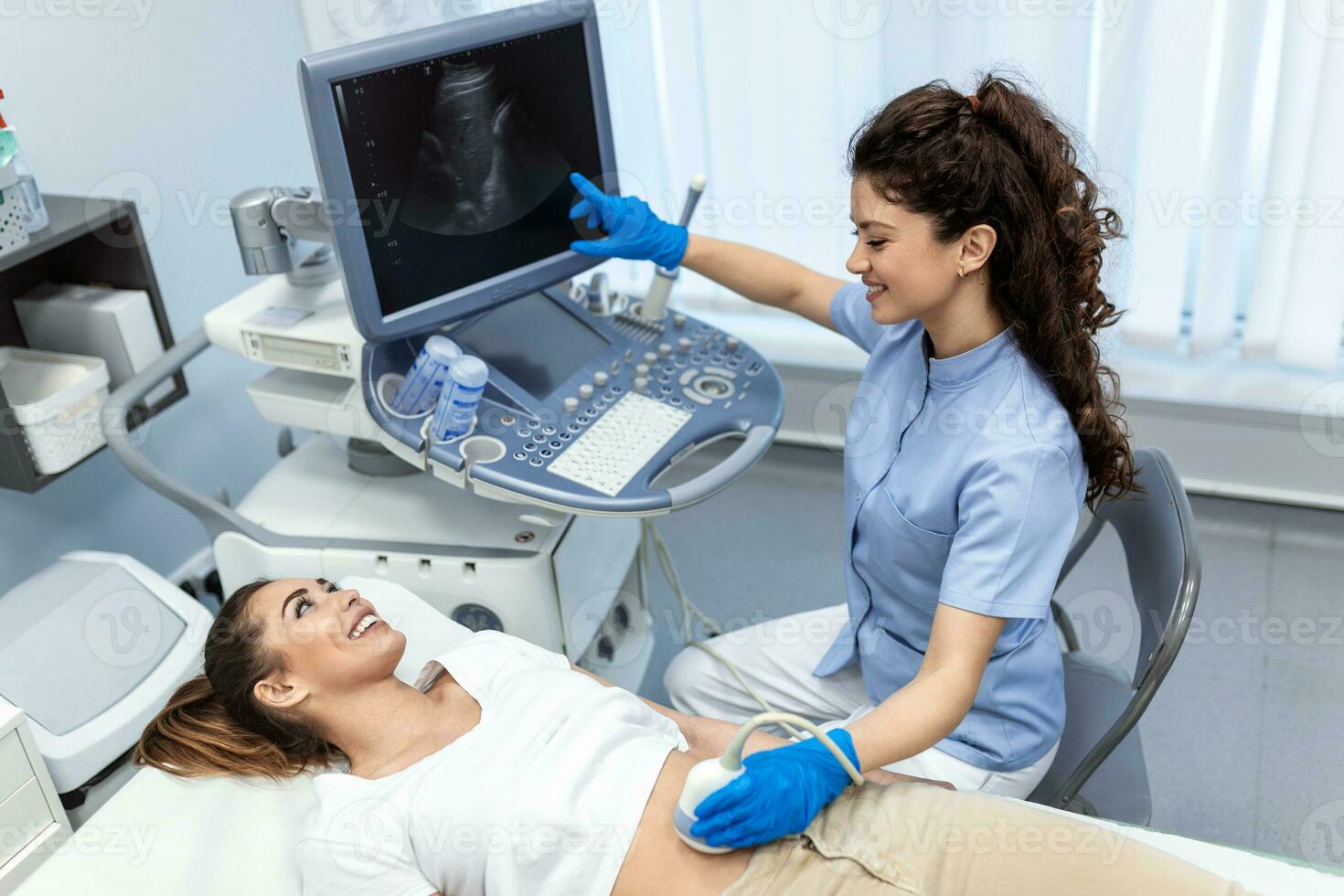 Ultrasound diagnostic of stomach on abdominal to woman in clinic, closeup view. Doctor runs ultrasound sensor over patient's girl tummy and looks at image on screen. Diagnosis of internal organs. photo