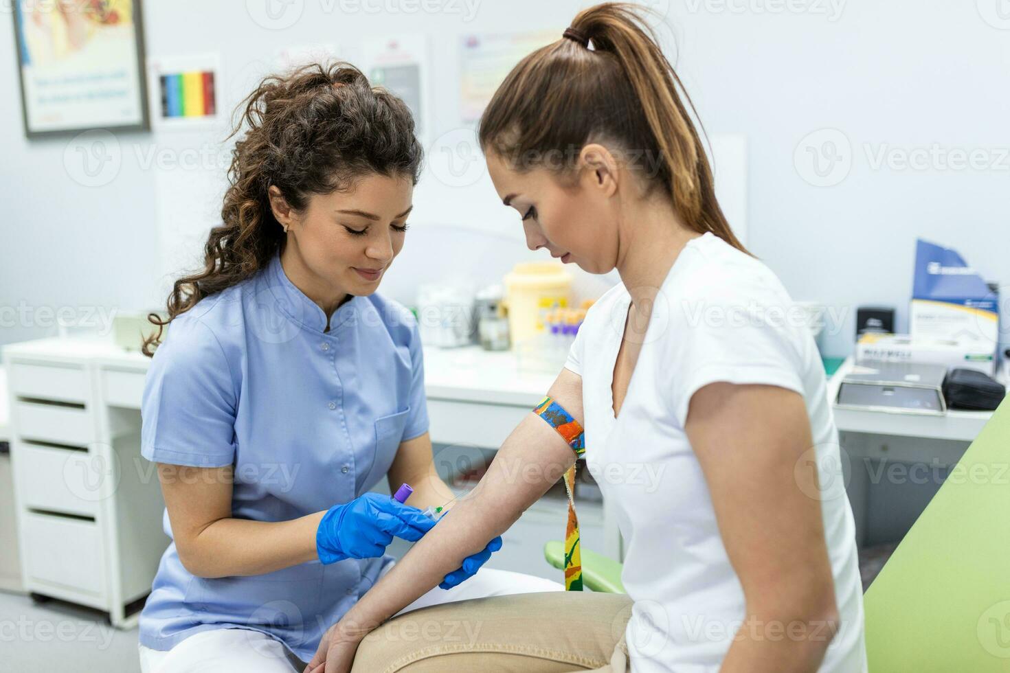 Preparation for blood test with pretty young woman by female doctor medical uniform on the table in white bright room. Nurse pierces the patient's arm vein with needle blank tube. photo