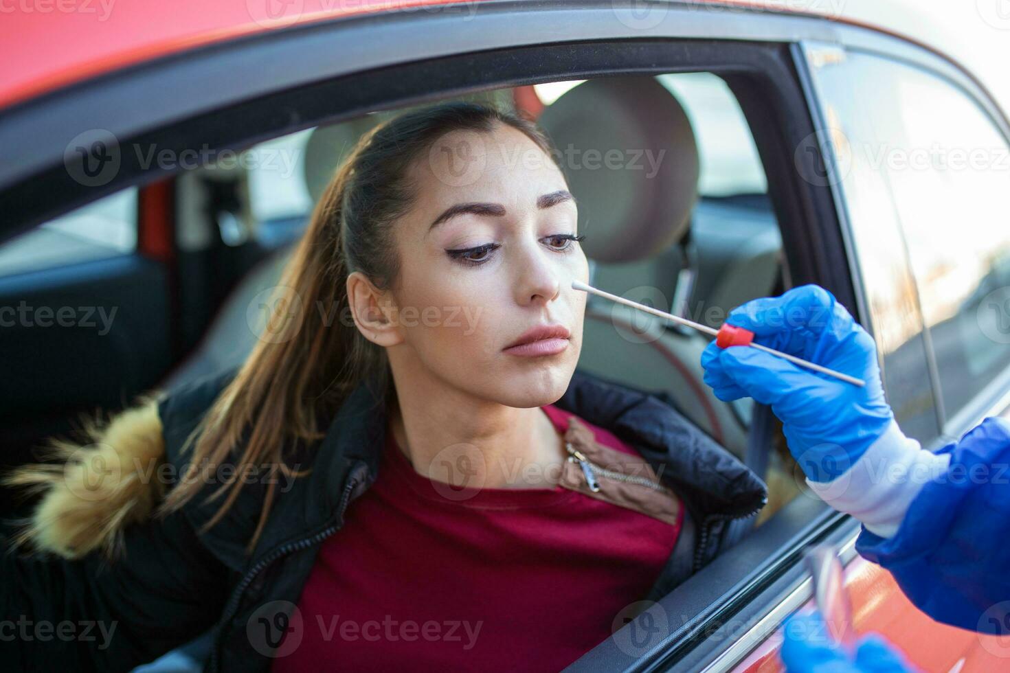 Woman getting tested at a coronavirus drive thru station by medical staff with PPE suit by throat swab. Health care drive thru service and medical concept photo