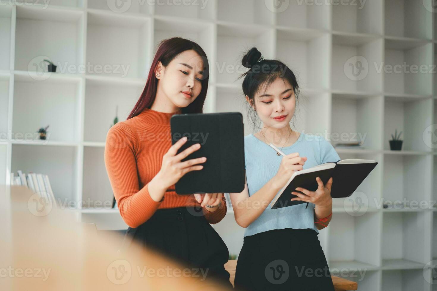 Two cheerful young multinational colleagues talking while standing in office with digital tablet, Business concept. photo