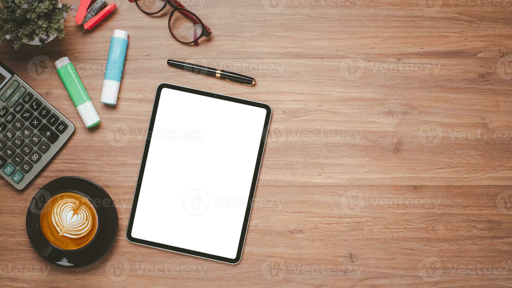 de madera escritorio lugar de trabajo con blanco pantalla digital tableta para producto mostrar, calculadora, lente, bolígrafo y taza de café, parte superior ver plano laico con Copiar espacio. foto