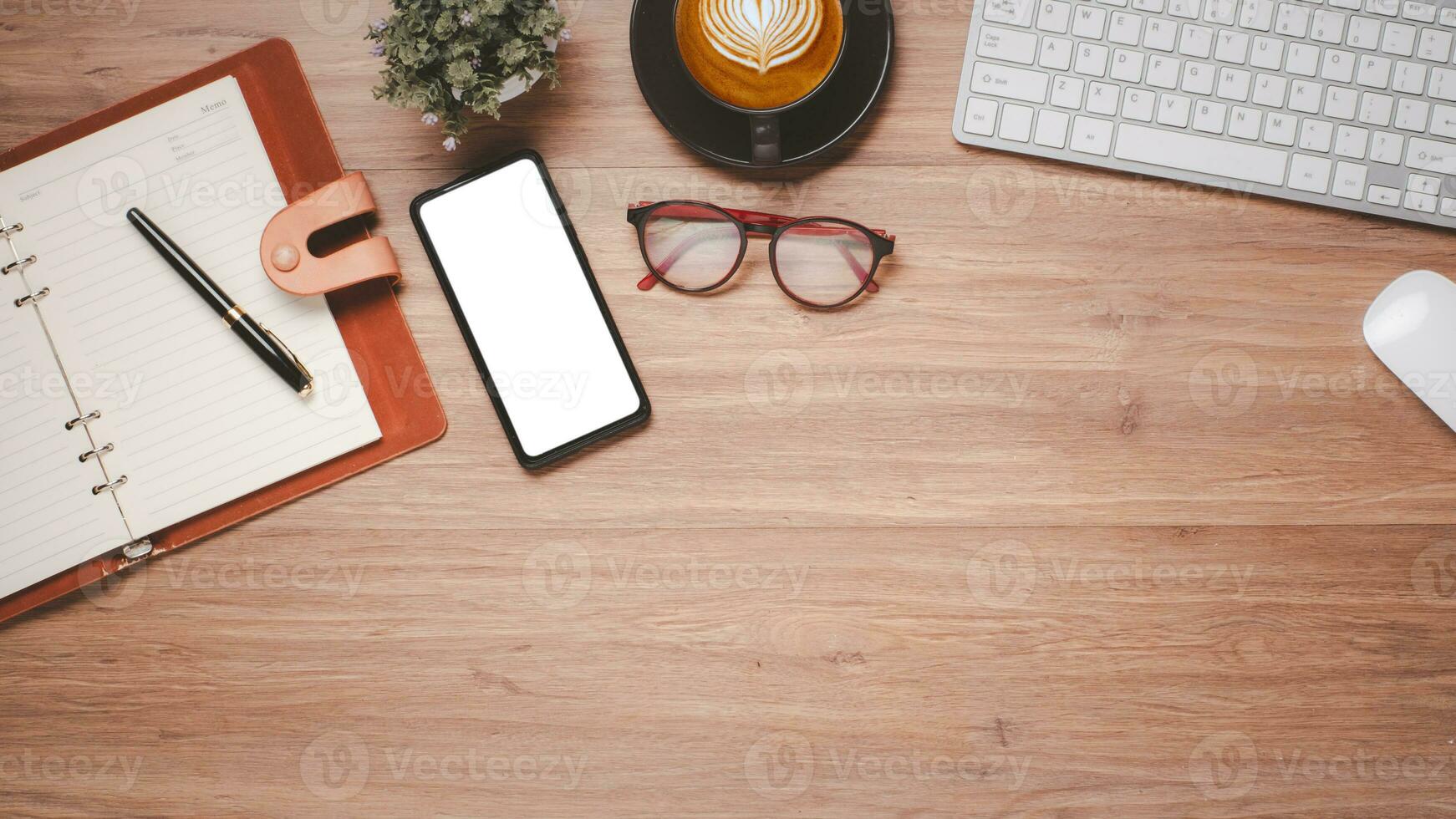 Wooden desk workplace with blank screen smart phone for product display, keyboard, mouse, eyeglass, notebook, pen and cup of coffee, Top view flat lay with copy space. photo