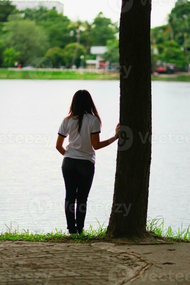 The young woman stands alone on the balcony of the mountain lodge in the morning to watch the sun rise with loneliness. A young woman traveler universe standing alone in loneliness by a reservoir. photo