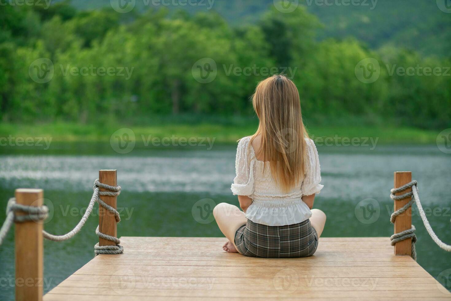 young woman sits alone on a path by a reservoir, lonely and depressed after living alone for so long. The back of a woman sitting by the reservoir alone in the evening and with a copy space for text. photo