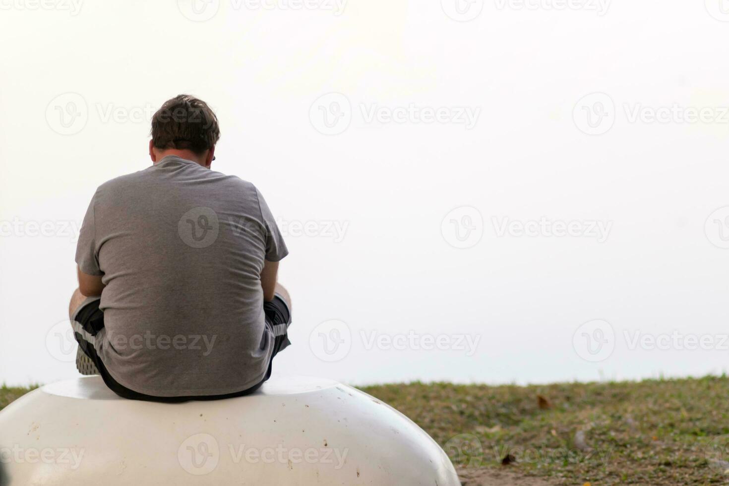 A depressed young man sat by the reservoir alone with a depressed feeling. The young man sat by the reservoir, depressed and staring into the water with emotional strain. Copy Space for text. photo