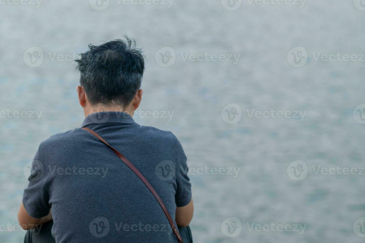 A depressed young man sat by the reservoir alone with a depressed feeling. The young man sat by the reservoir, depressed and staring into the water with emotional strain. Copy Space for text. photo