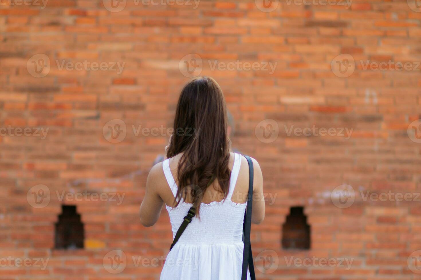 Asian tourists traveling and taking in sights of ancient city wall in Chiang Mai, Thailand, alone in summer. Back view of young female tourist taking walk taking in view of city wall and copy space photo