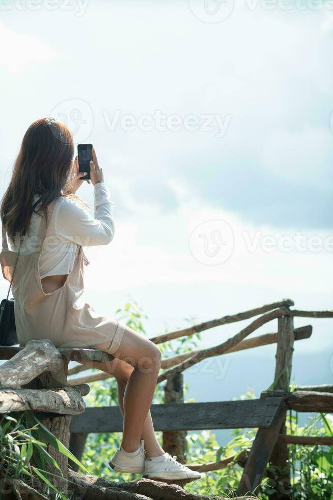 Back view of young woman sitting on long bench alone in evening looking at beautiful summer landscape background of nature and with copy space for text. concept loneliness of woman who is alone photo