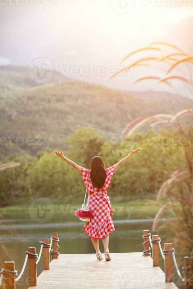 old woman stand on walkway by reservoir watching beautiful scenery of reservoir alone in the evening. back of old woman stand by reservoir alone in evening and with copy space for text. photo