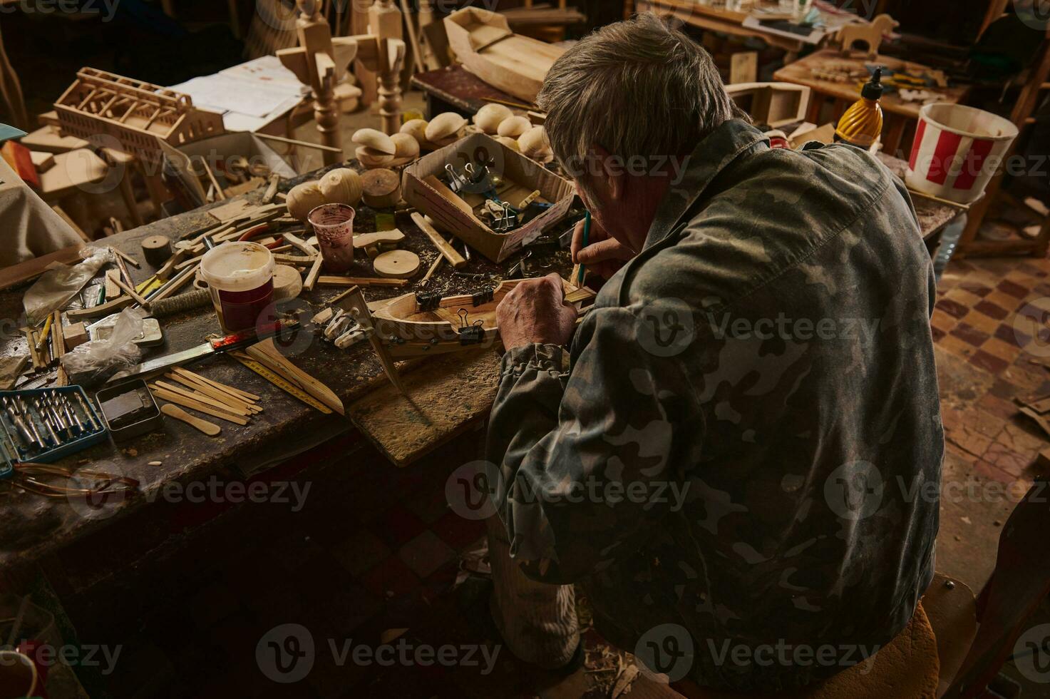 Rear view of an old craftsman making a wooden model of sailship in his home workshop. Carpenter at work photo