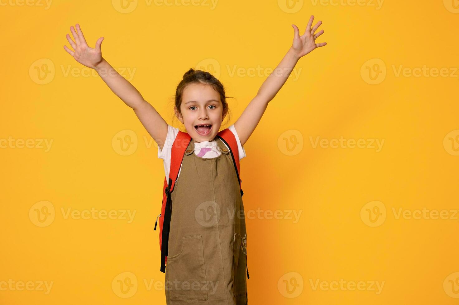 Authentic portrait of a schoolgirl in casual wear, expressing positive emotions, isolated over orange studio background photo