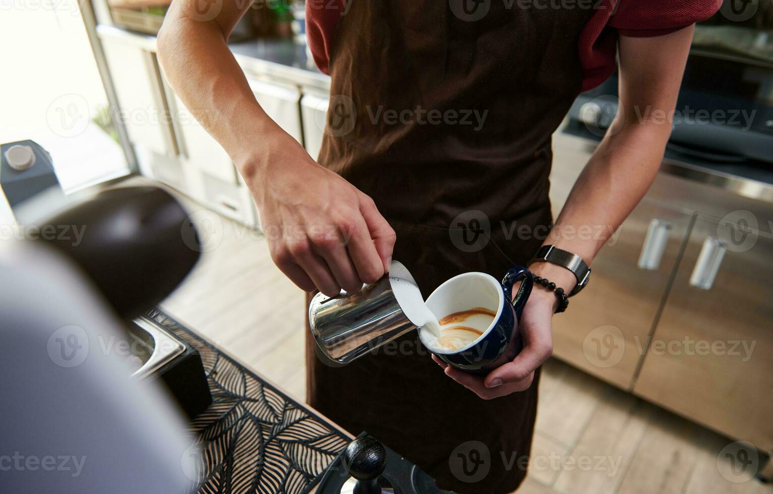 Close-up of professional barista pouring steamed milk into coffee cup making latte behind bar counter photo