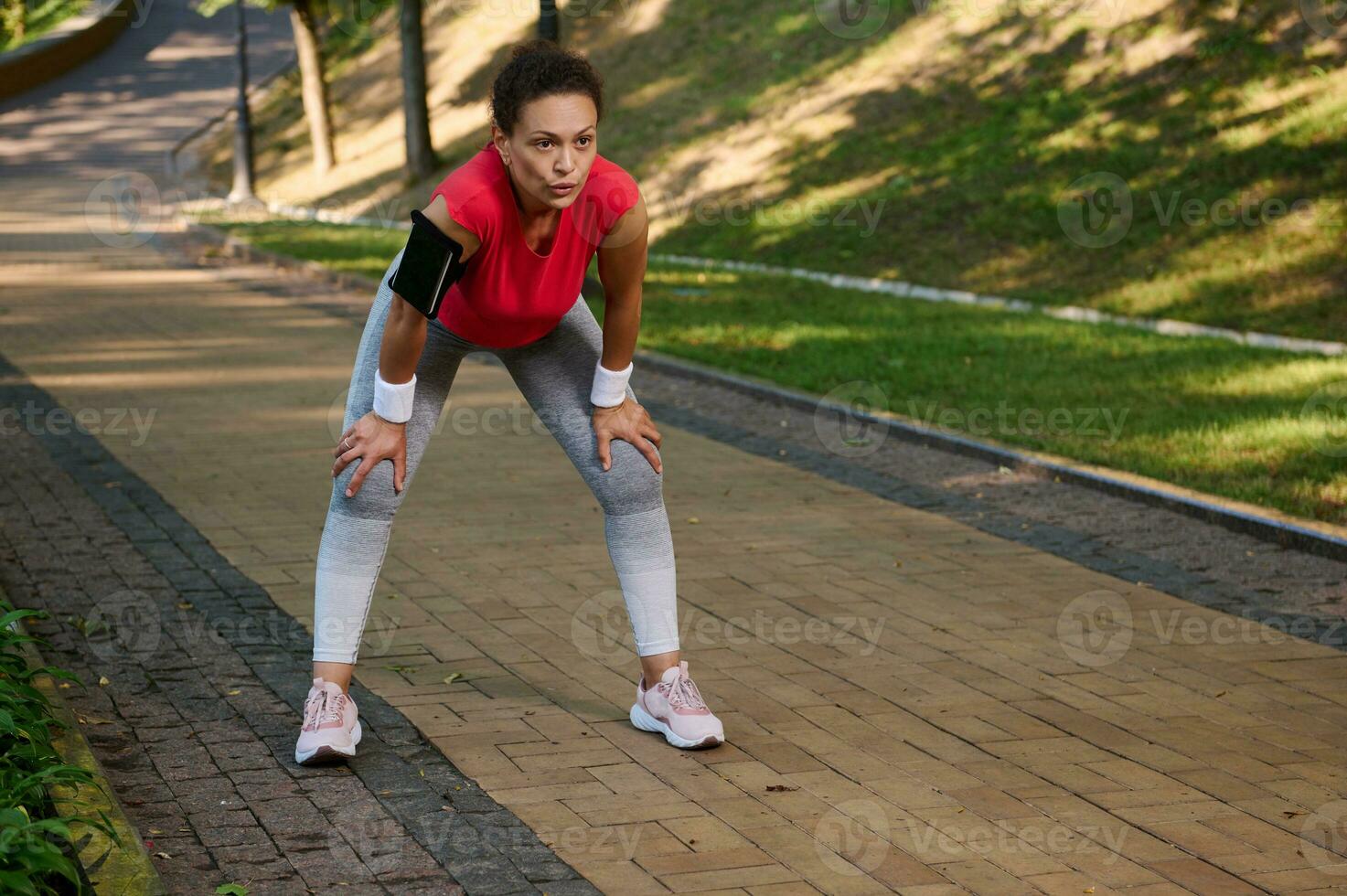 Female runner, Latin American sportswoman feeling exhaustion while jogging on the running track or treadmill in the city park. Active lifestyle, body weight training, slimming and dieting concept photo