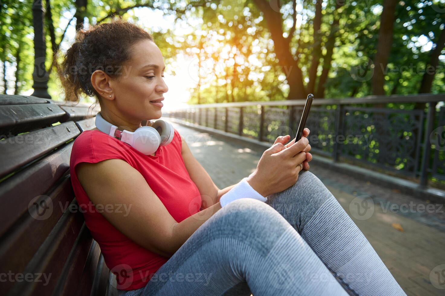 Middle-aged African woman in sportswear using mobile phone for sending text message, checking fitness mobile application photo