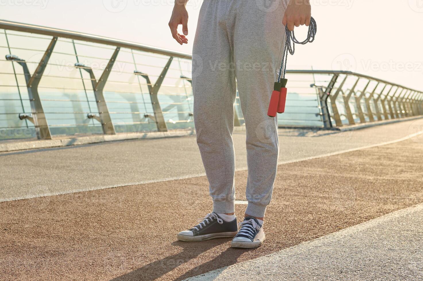 Cropped view of a sportsman holding a jumping rope while standing on a treadmill during a morning cardio workout photo