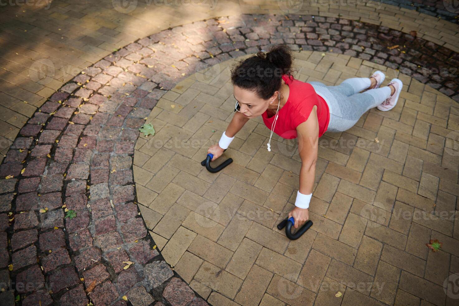 Overhead view of a sporting woman exercising outdoor doing push ups in the city park during morning workout on the summer day photo